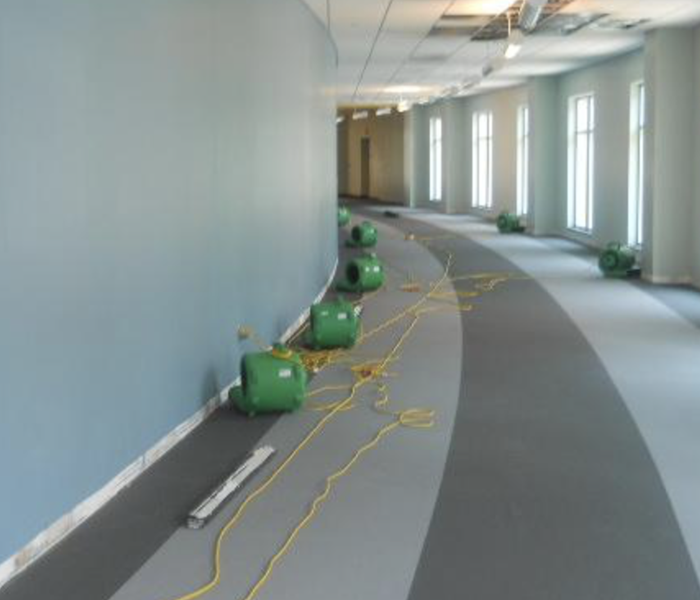 Green SERVPRO air movers on floor in a large hallway.