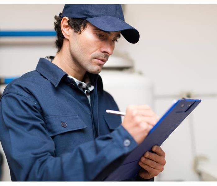 A plumber in a blue cap writing on a clipboard